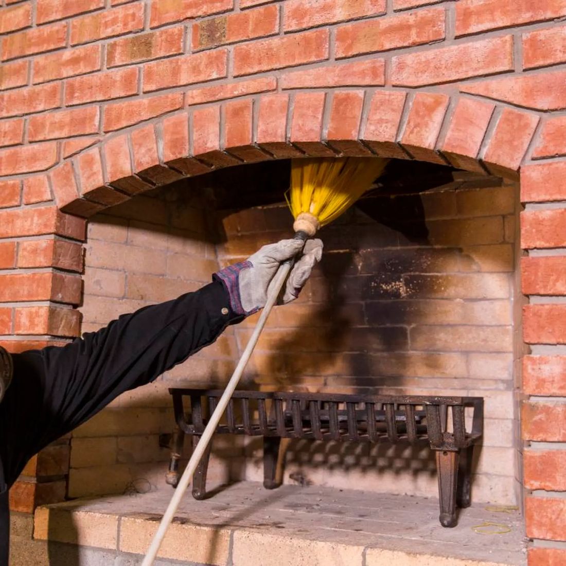Chimney sweep brushing a fireplace flue from inside the firebox